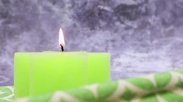 Komposition mit einer grün beleuchteten brennenden Kerze auf einem Tisch mit einer grünen Leinenserviette auf einem schönen grauen Marmorhintergrund. Platz für Ihren Text. Weihnachtsdekorationen. video