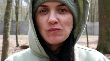 Close-up of a happy smiling woman chewing, eating and enjoying the taste. A girl in a hat and a hood in a spring forest against a background of trees. Slow motion. video