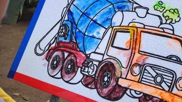 un' bambino è colorazione un' immagine di un' polistirolo camion, nel un' parco video