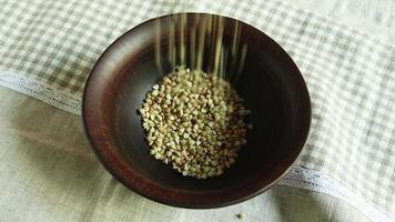 Pour raw green buckwheat into a plate. Fresh green buckwheat kernels fall into a clay brown bowl, close-up. Raw Healthy Organic Diet. The concept of healthy vegetarian eco food, diet.