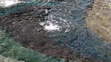 frecuentes gotas de agua en una fuente en cámara lenta caen sobre una superficie de agua limpia con salpicaduras y burbujas. chorros de agua brillan bajo el sol. el spray se extiende lentamente hacia los lados. de cerca. video