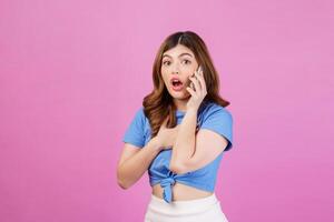 Portrait of excited young woman wearing casual t-shirt talking on mobile phone isolated over pink background photo