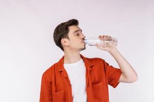 Portrait of Happy young man drinking water from a bottle and looking at camera isolated over white background photo