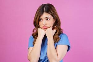 retrato de una mujer pensativa, miserable y abatida, con una camiseta informal, manteniendo las manos bajo la barbilla, aislada sobre un fondo rosado foto