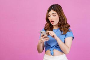 Portrait of excited young woman wearing casual t-shirt using smartphone isolated over pink background photo