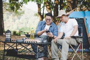 amigos hombres sentados en una silla en el campamento hablando y mirando el teléfono inteligente foto