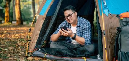 Portrait of Asian traveler man glasses using smartphone in tent camping photo