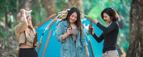 Young women cheer and drink beverage  front of camping tent photo