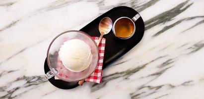 Top view or Flat lay of glass of vanilla ice cream with stainless mug espresso mug shot, copper tea spoon and red plaid cotton in black tray on white marble table with copy space - Affogato coffee photo