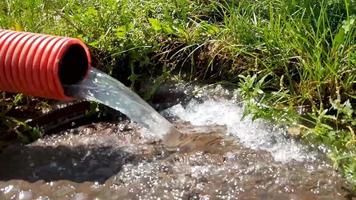 water from a red corrugated pipe flows down the drain. Water is flowing. Rain water flows out of the pipe and falls down. Wastewater flows into the external sewer. Pumping water with a pump video