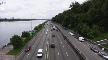 Cars drive along the embankment of the highway in Kiev, Ukraine. Traffic in both directions on a busy road. Aerial view of cityscape. Ukraine, Kiev - June 1, 2020. video
