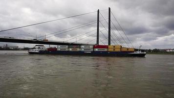 en transport fartyg levererar varor och behållare längs de Rhen längs Düsseldorf på en grå, kall dag. theodor hoyce brucke är en bro. statisk video. Düsseldorf, Tyskland - februari 19, 2020. video