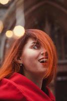 Cierra a una joven emocionada con abrigo rojo en una foto de retrato de la ciudad