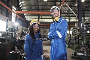 dos equipos de trabajadores industriales con uniformes de seguridad con brazos cruzados confiados, colegas ingenieros, trabajan con máquinas metalúrgicas en la fábrica de fabricación. carrera de mecanica de produccion profesional. foto