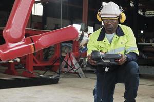 An African American production engineer test and control robotic arm in mechanical manufacturing factory, intelligent automatic machines in industrial business, and futuristic technology innovation. photo