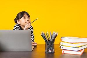 niña joven que piensa como aprender en una computadora portátil con fondo amarillo, estudiar, buscar y videoconferencias en coronavirus y covid 19 tiempo de propagación