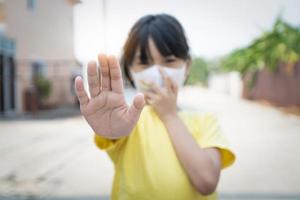 Young Asian girl wearing mask for protect covid 19, Thai kid wear dust mask. for protect pm2.5 and show stop hands gesture for stop corona virus outbreak. photo