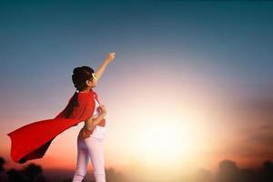Super girl child show power,little kid wearing red hero cloak show hand up to sky in sun set, active dream and motivation idea concept
