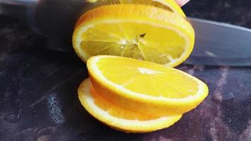 eine weibliche hand schneidet mit einem messer runde scheiben saftiger orange auf dem tisch. Hausfrau in der Küche zu Hause, die frische Orangenfrüchte auf einem Schneidebrett schneidet. das konzept der gesunden ernährung, des kochens. video