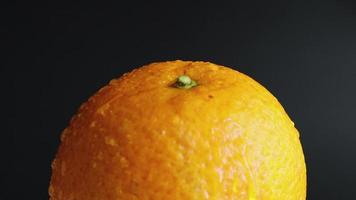 statisch nicht bewegte nasse und nasse ganze Orange mit Wassertropfen auf einer leuchtend orangefarbenen Schale auf schwarzem Hintergrund. Früchte für Ernährung und gesunde Ernährung. Zitrusfrüchte, Seitenregen, tropische Früchte aus nächster Nähe. video