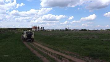 Rear view of a small four-wheel drive car looking at a dusty road in the steppe, driving along a route near a field on an empty rural road in the countryside on a summer day. video