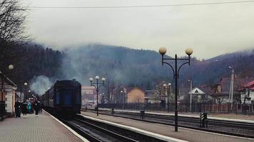 a estação ferroviária, um trem passa, nas montanhas de fundo. os passageiros saem do trem na plataforma de uma pequena estação em uma cidade pouco povoada. ucrânia, yaremche - 20 de novembro de 2019. video