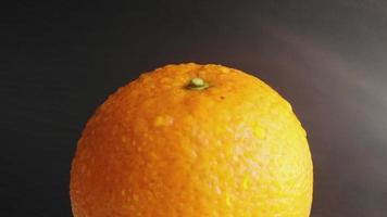 Static still wet all orange close-up with splashes of water, 4k video with drops of water on a bright orange peel, on a black background. Citrus fruits, side rain, tropical fruits close-up.