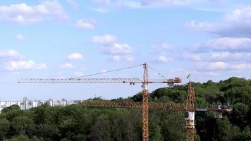 lavoratori costruzione Torre sollevamento alto giallo gru su un' moderno edificio sotto costruzione contro nuvoloso cielo e città. urbano sviluppo e costruzione concetto. industriale sfondo. video