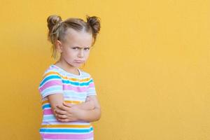 niña pequeña y seria que parece infeliz ante la cámara, molesta a un niño preescolar melancólico o aburrido, aislada sobre el fondo amarillo del estudio foto