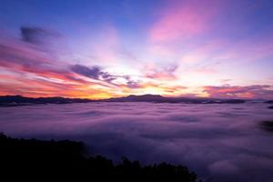 Aerial view of flowing fog waves on mountain tropical rainforest,Bird eye view image over the clouds Amazing nature background with clouds and mountain peaks in Thailand photo