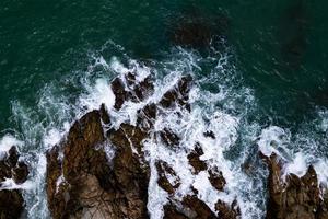 increíble vista superior hermosa costa, vista aérea rompiendo olas en las rocas, superficie oscura del mar costa rocas acantilados fondo foto