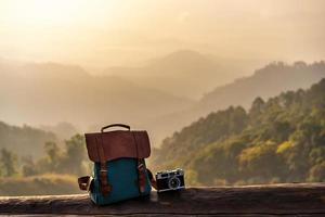 Travel backpack and retro camera with landscape view of mountain at sunrise photo