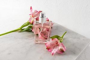Beautiful bottle of women's perfume or spray against the background of pink flowers and marble white slab. presentation of the aroma. top view. photo