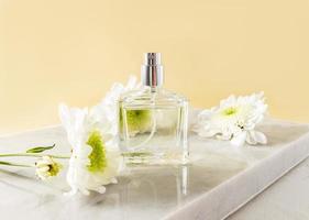 A beautiful bottle of women's perfume or spray stands on a white marble podium with white flowers. front view. An empty layout for your fragrance. photo