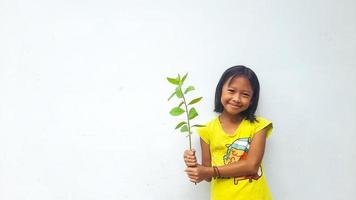 Little girl holding young plant.  Green Leaves. Ecology concept. Light color background. photo