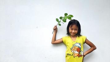 Little girl holding young plant.  Green Leaves. Ecology concept. Light color background. photo