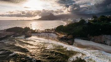 Aerial drone view above Praia do Diabo, Arpoador and Ipanema Beaches in Rio de Janeiro, Brazil on a cloudy day with many Cariocas enjoying the beaches