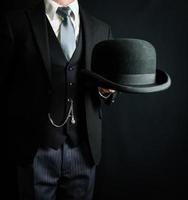 retrato de mayordomo con traje oscuro sosteniendo un bombín. estilo vintage y moda retro del clásico caballero británico. foto