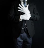 retrato de mayordomo en traje oscuro sobre fondo negro tirando de guantes blancos limpios. concepto de industria de servicios y hospitalidad profesional. foto