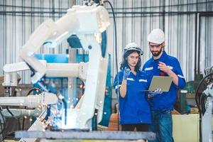 Engineers team mechanic using computer controller Robotic arm for welding steel in steel factory workshop. Industry robot programming software for automated manufacturing technology photo
