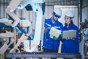 Two engineers mechanic using computer controller Robotic arm for welding steel in steel factory workshop. Industry robot programming software for automated manufacturing technology photo