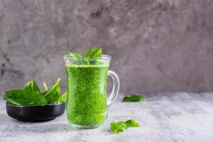 Fresh spinach smoothie in a glass and a bowl with leaves on the table. Natural antioxidant. photo