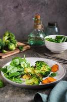 Fried broccoli, carrots and spinach leaves on a plate. Healthy food. Vertical view photo