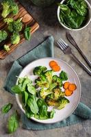 brócoli a la parrilla y zanahorias y hojas de espinacas en un plato. dieta vegetal. vista superior y vertical