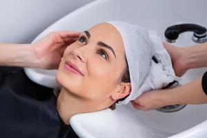 peluquero profesional lavando el cabello de una mujer joven en un salón de belleza foto