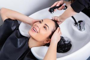 peluquero profesional lavando el cabello de una mujer joven en un salón de belleza foto