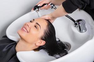 peluquero profesional lavando el cabello de una mujer joven en un salón de belleza foto