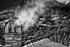 A black and white mountain house roof with smoking chimney photo