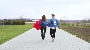 Liebe. Junger Mann umarmt und küsst ein Mädchen im Park mit roten Luftballons video