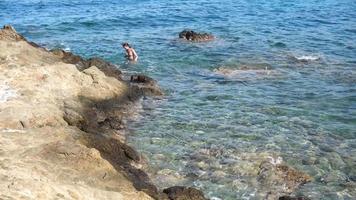 jovem alegre nada na praia rochosa selvagem video